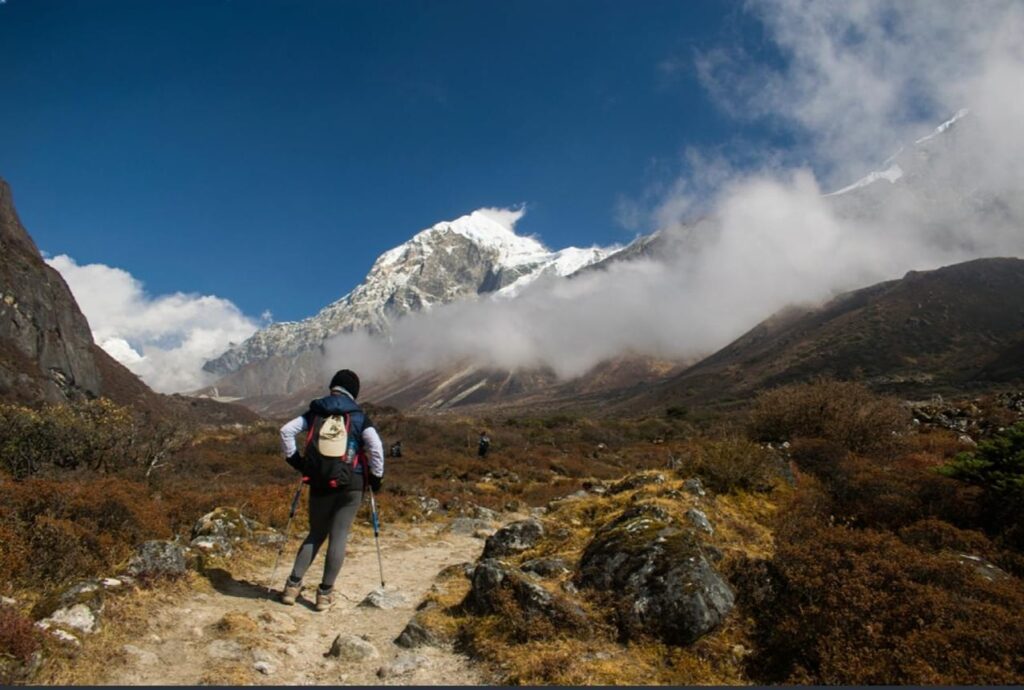Trekker walking on the Goechala Trek trail with snow-covered mountains and clouds in Sikkim